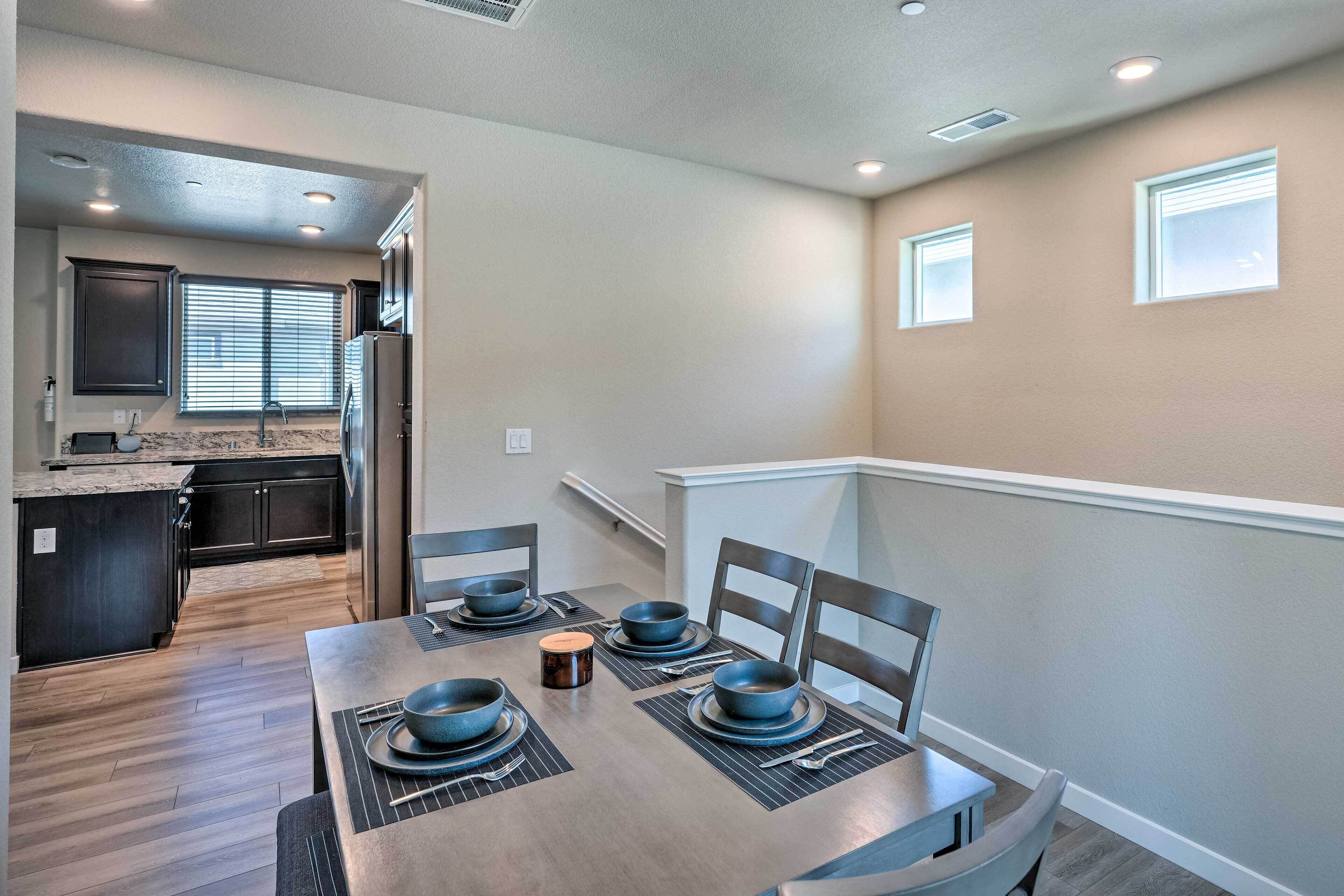 Un comedor con una mesa de madera dispuesta para cuatro, una cocina al fondo y una escalera que lleva a un nivel superior.