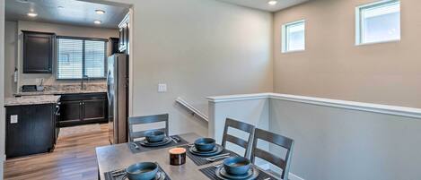 Un comedor con una mesa de madera dispuesta para cuatro, una cocina al fondo y una escalera que lleva a un nivel superior.
