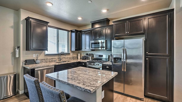 A modern kitchen with dark cabinetry, stainless steel appliances, and a granite island.
