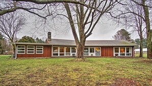 Ein Bungalow mit großer Veranda, Schornstein und Baum davor.