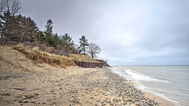 Ein kiesiger Strand mit einer Holzbrüstung und Bäumen im Hintergrund.