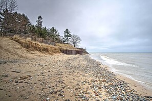 Una playa de canto mezclado con una valla de madera y árboles al fondo.