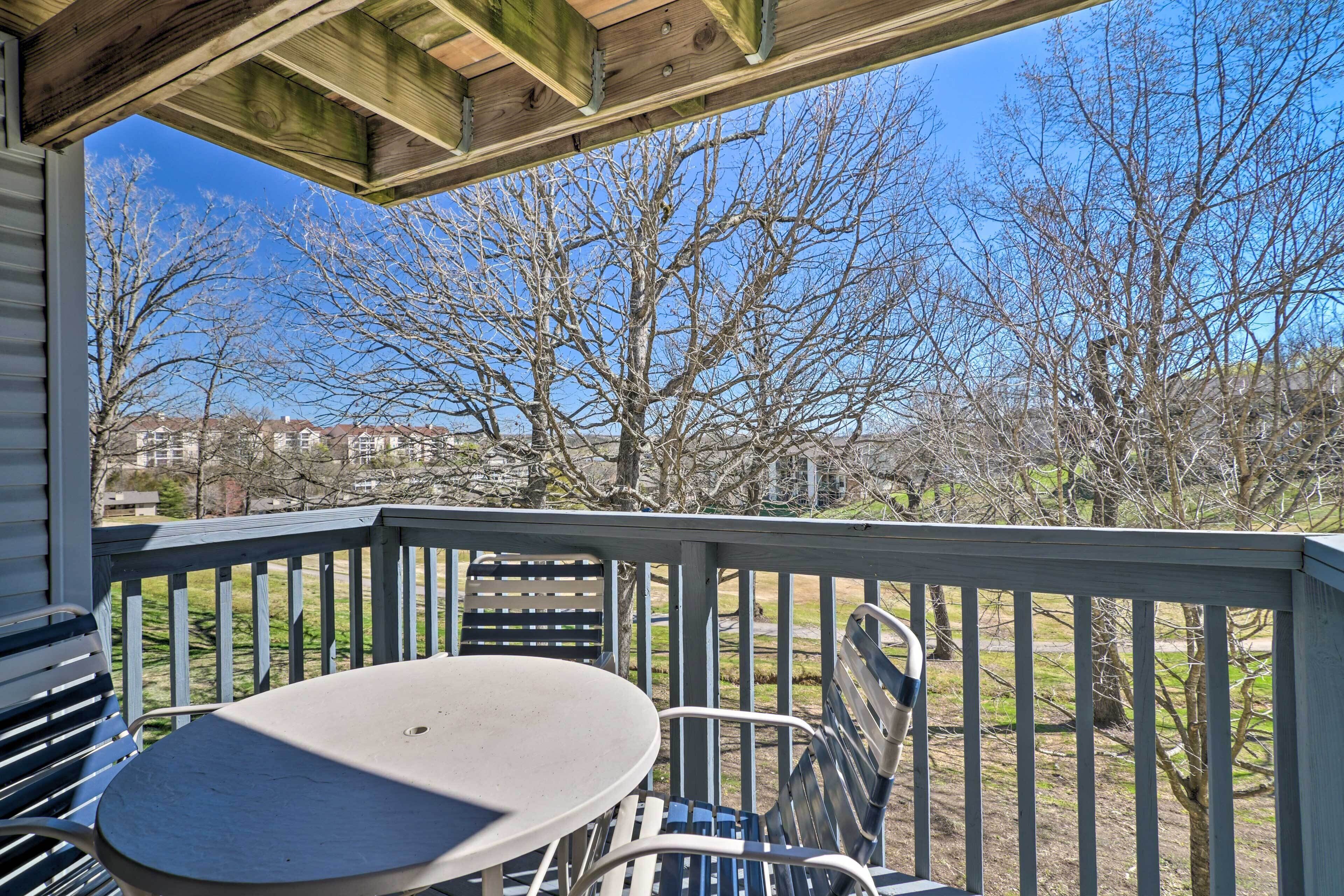 A covered outdoor area with a table and chairs, a wooden ceiling, and a view of leafless trees and houses in the background.