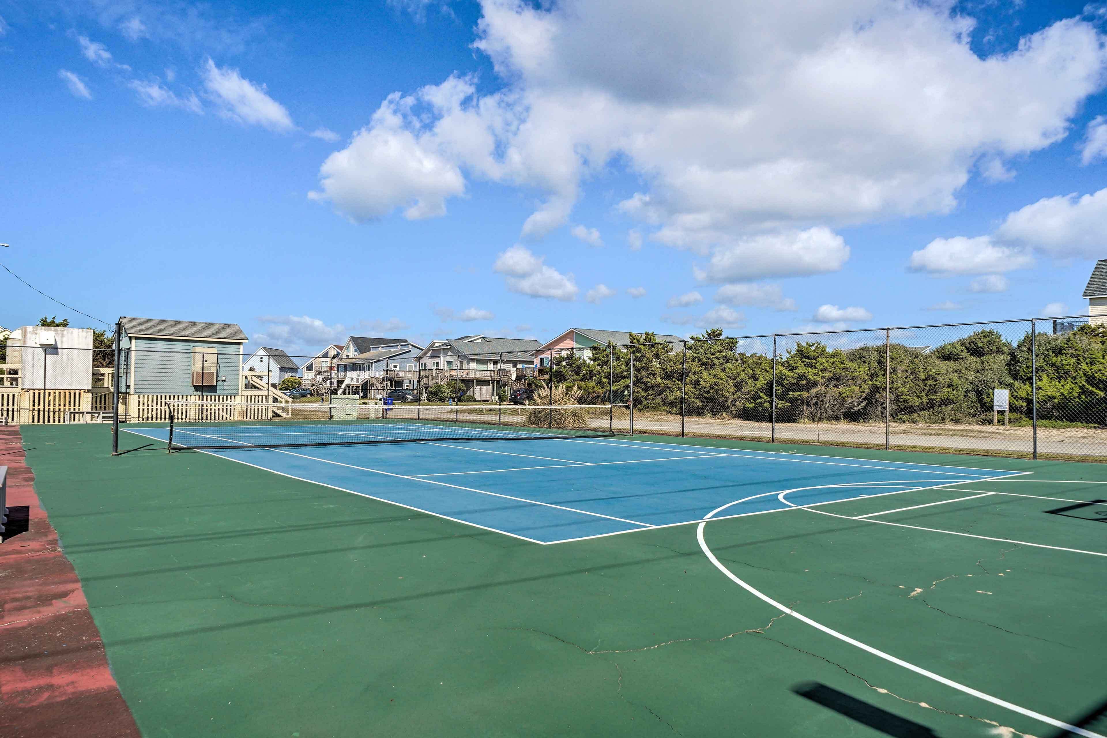 Un court de tennis en plein air, doté d’une surface verte, entouré d’une clôture grillagée et avec des immeubles d’habitation en arrière-plan.