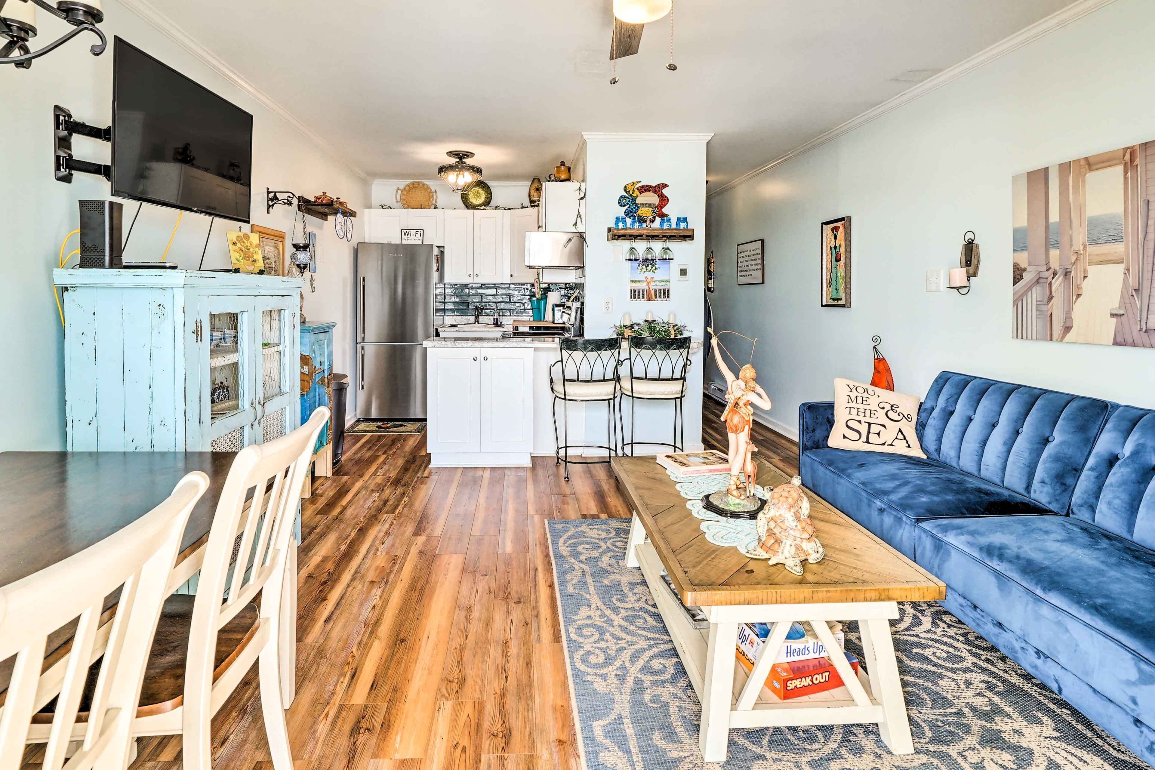 A modern kitchen with white cabinets, a central island, and a dining area with a blue sofa and wooden table.