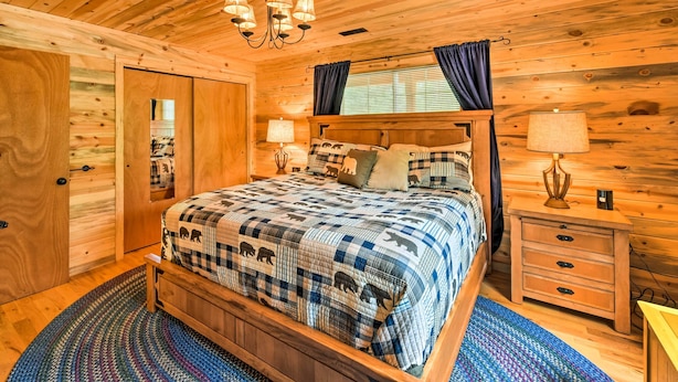 A wooden cabin bedroom with a bed, nightstands, and a chandelier. - 'bobcat Trail Cabin' on 3 Acres in Como! (Como)