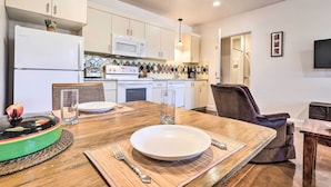 A modern kitchen with white cabinets, a microwave, and a stove. There is a dining table with a plate and cutlery, and a chair. - Quaint Kanab Casita - 3 Mi to the Heart of Town! (Kanab)