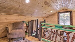 A wooden interior with a plush armchair, a wooden staircase with a rustic railing, and a window with a view of greenery. - Rustic Hendersonville Farm Studio w/ Private Deck (Hendersonville)