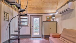 A room with a spiral staircase, a sofa, a cabinet, and a door leading outside. - Rustic Hendersonville Farm Studio w/ Private Deck (Hendersonville)