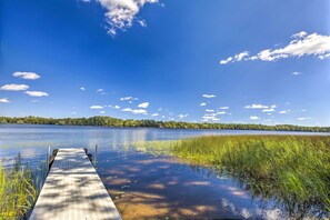 A wooden dock extending into a calm lake with surrounding greenery and a clear blue sky. - A-frame Cabin w/ Private Boat Dock! (Butternut)