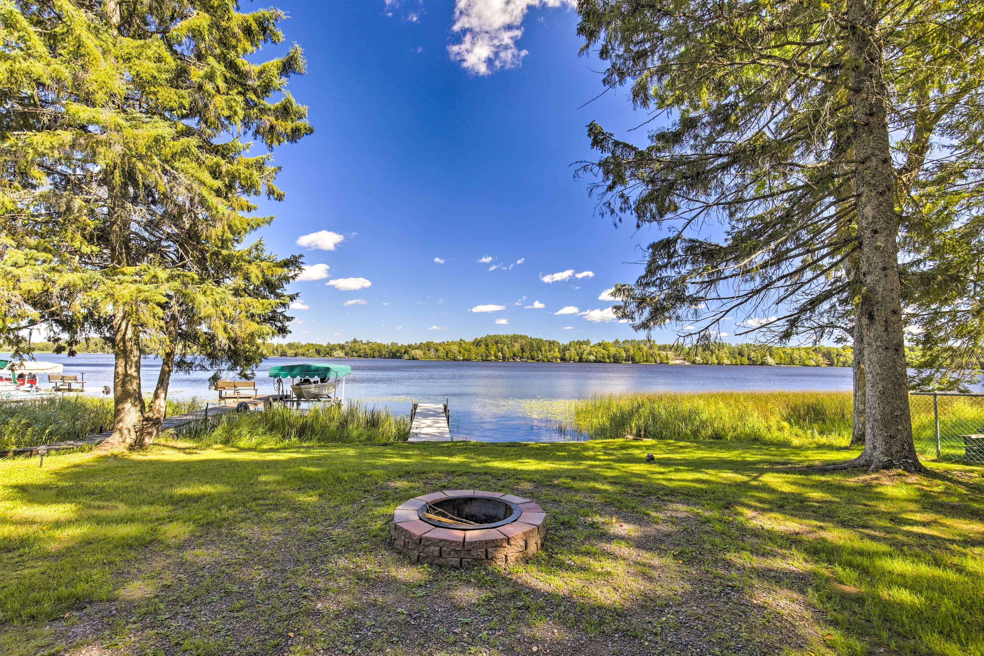 A lakeside setting with a fire pit, dock, and grassy area.