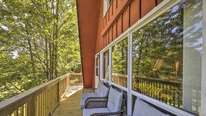 Une terrasse en bois, agrémentée de chaises et de coussins en osier, qui offre une vue sur une autre terrasse en bois et sur des arbres.