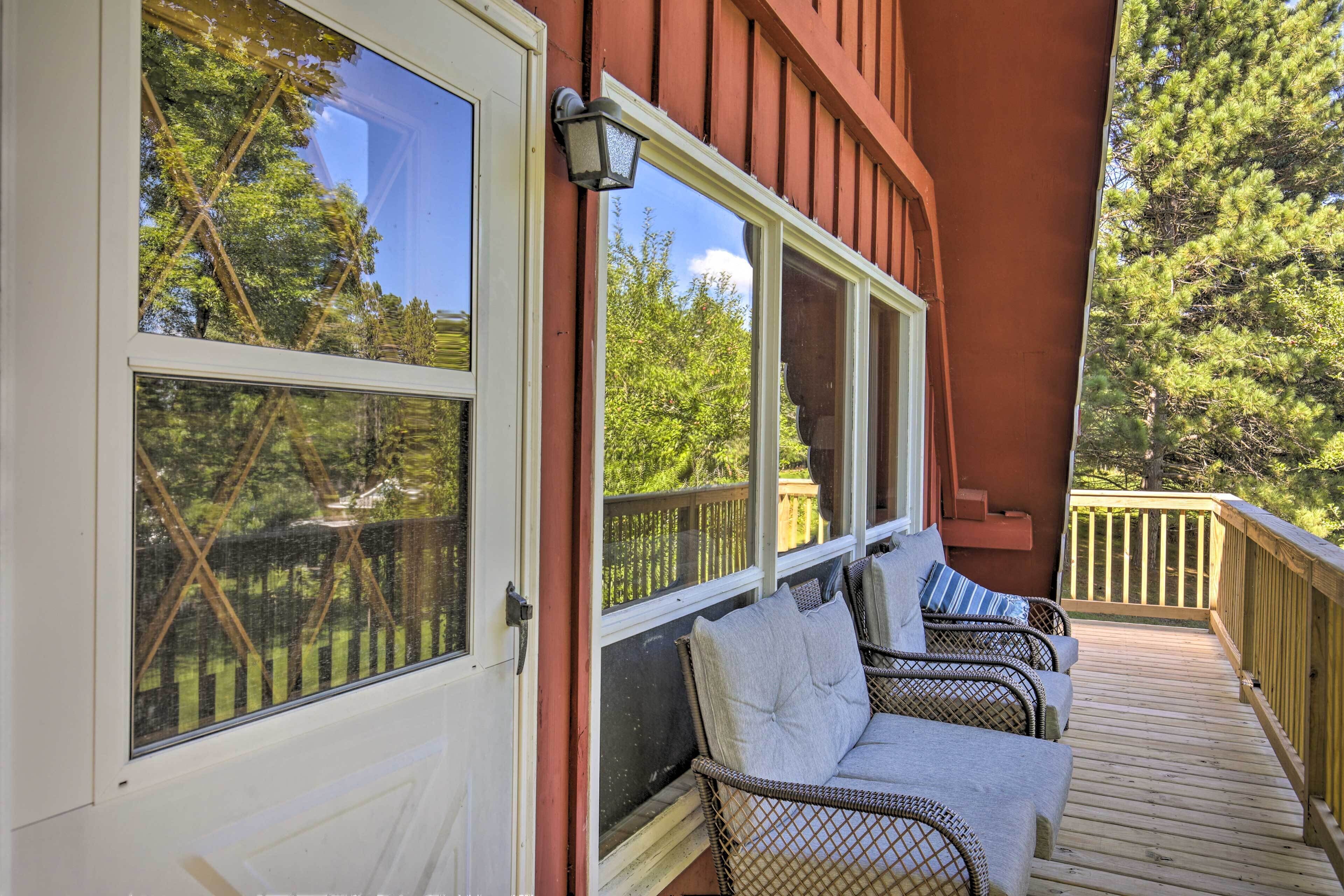 A covered porch with wicker furniture and a view of the surrounding trees.