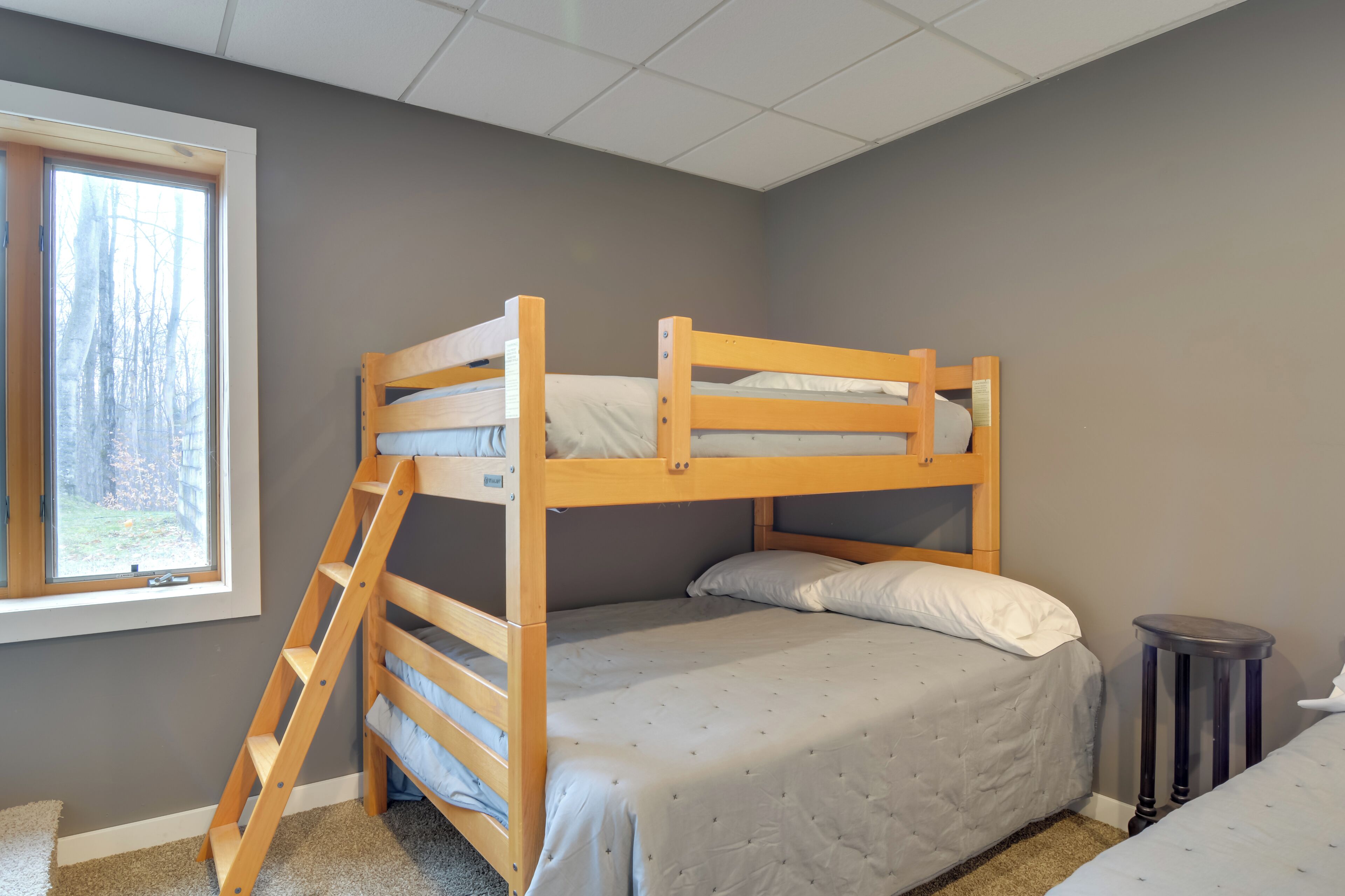 Een slaapkamer met een stapelbed, een raam, een klein krukje en een prullenbak.