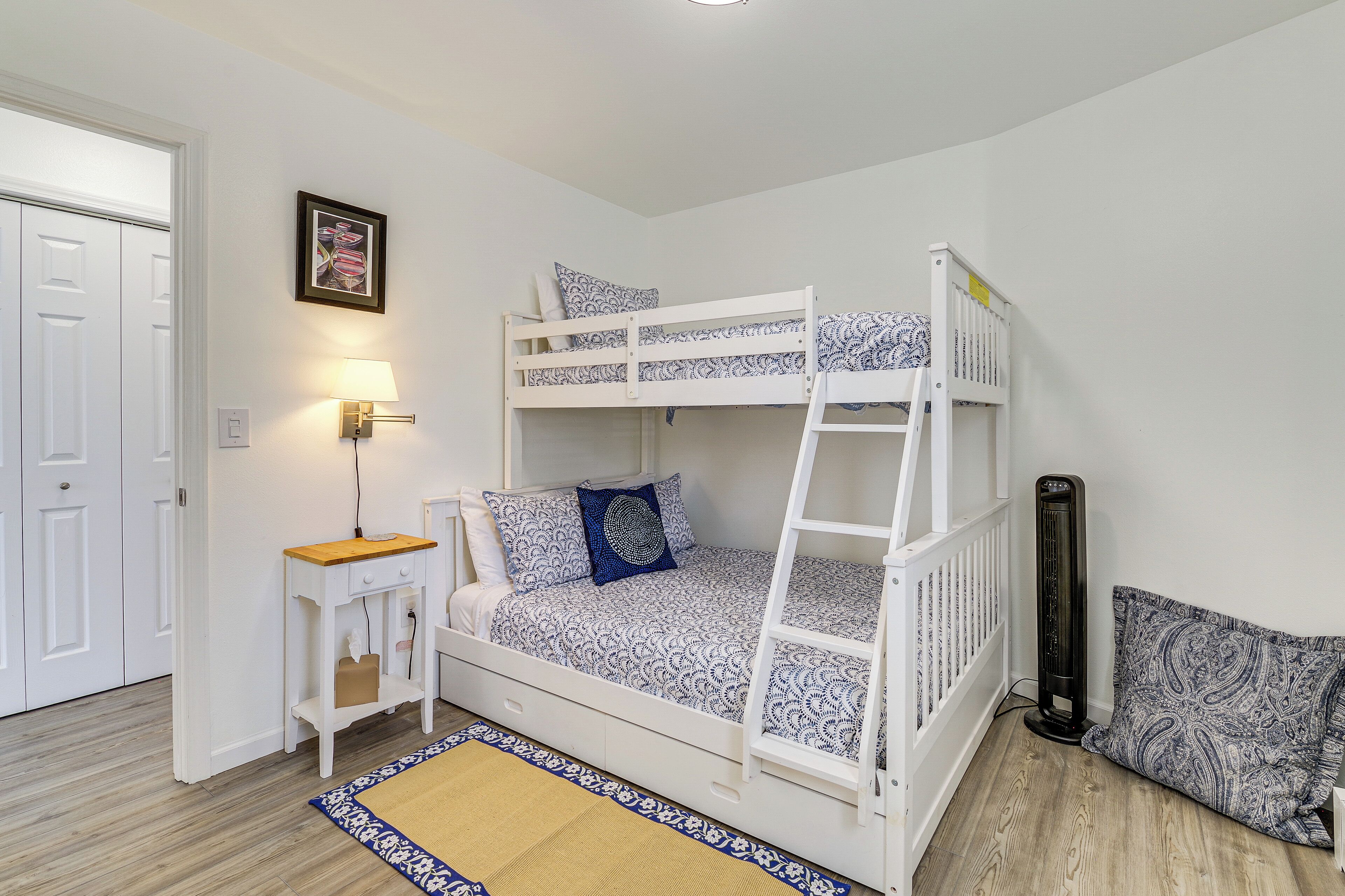 A bunk bed with a ladder, a bedside table, a lamp, and a patterned rug.