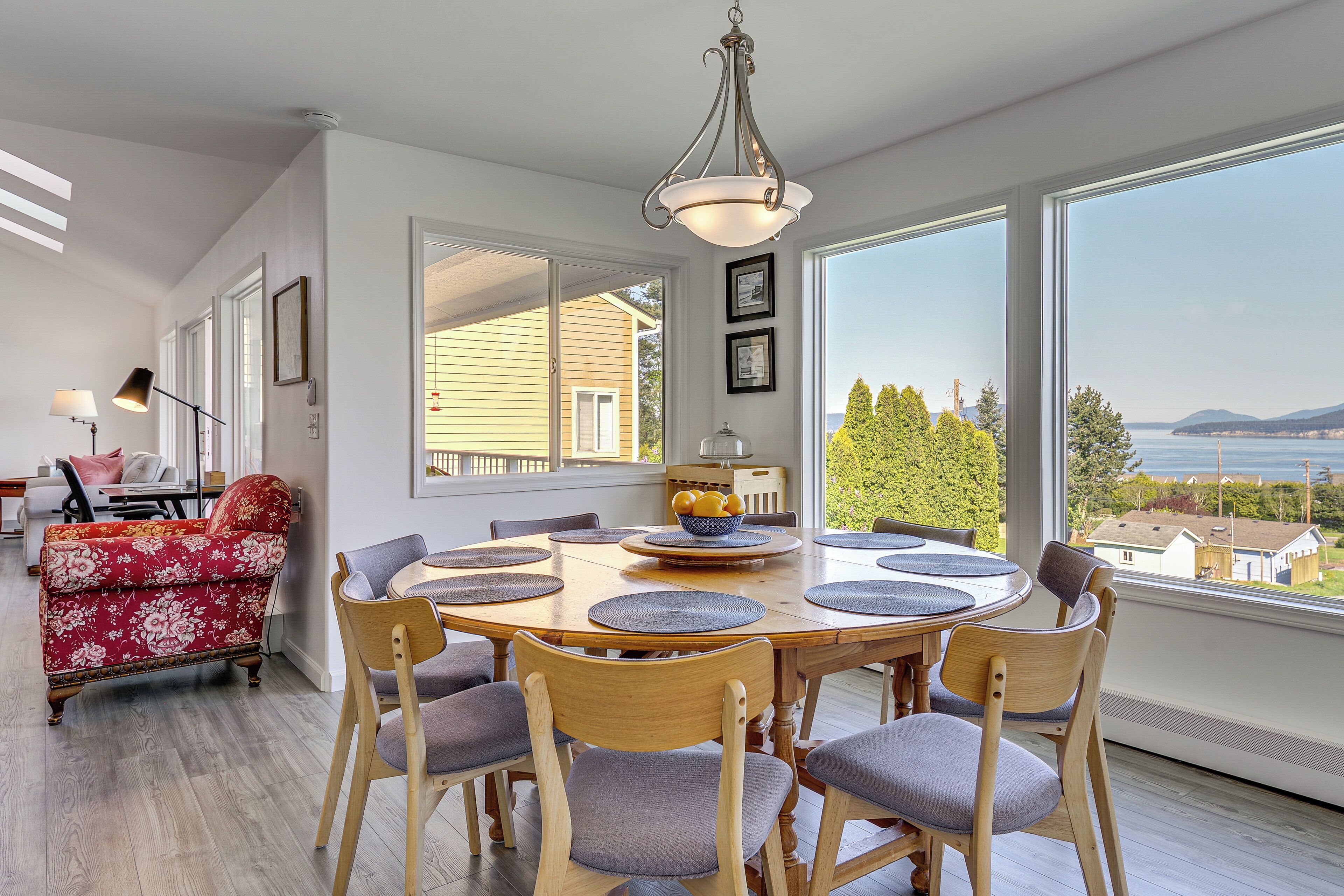 A dining area with a wooden table and chairs, a red floral sofa, and a view of the ocean.