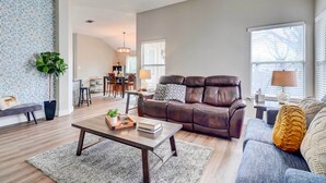 A living room with a brown leather sofa, a blue sofa, a coffee table, and a dining area with a chandelier. - Airy Georgetown Home w/ Fire Pit! (Georgetown)