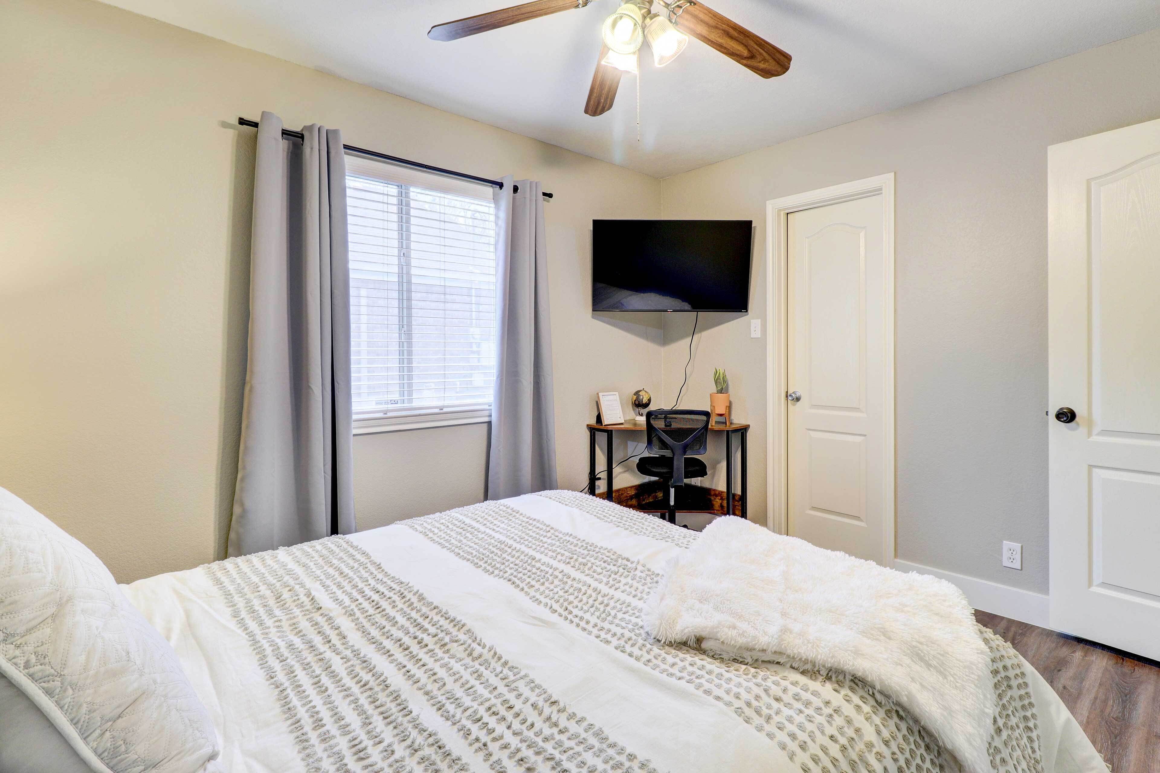 Ein Schlafzimmer mit Bett, Deckenventilator, Fernseher und Schreibtisch mit Stuhl.