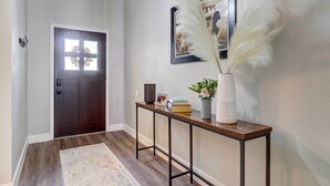 A hallway with a dark wooden door, a small table with a vase and books, and a framed picture on the wall. - Airy Georgetown Home w/ Fire Pit! (Georgetown)