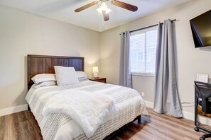 A bedroom with a wooden headboard, a bed with white bedding, a ceiling fan, a window with curtains, and a TV on a stand. - Airy Georgetown Home w/ Fire Pit! (Georgetown)