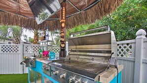 Une cuisine extérieure équipée d’un barbecue, d’un évier et d’une hotte en acier inoxydable.