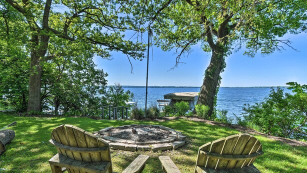 A wooden table and two Adirondack chairs in a grassy area with a fire pit, overlooking a lake and a dock. - Pet-friendly Family Home Situated on Green Lake! (Green Lake)