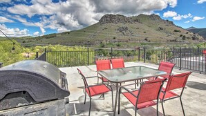 Een terras buiten met een glazen tafel en rode stoelen, met uitzicht op een bergachtig landschap.
