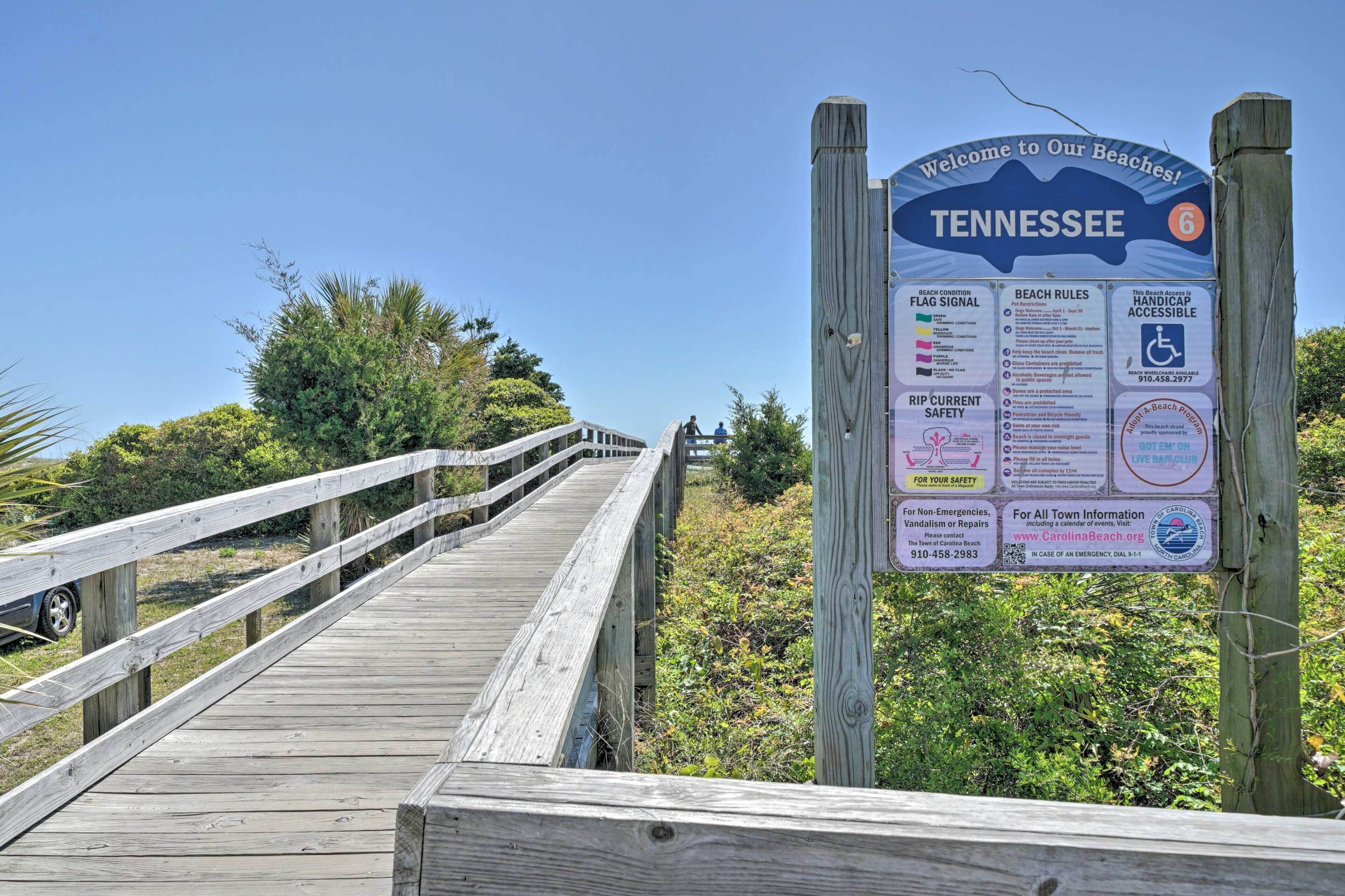 Un muelle de madera que conduce a una zona de playa, con un cartel que muestra normas de seguridad e información sobre la playa.