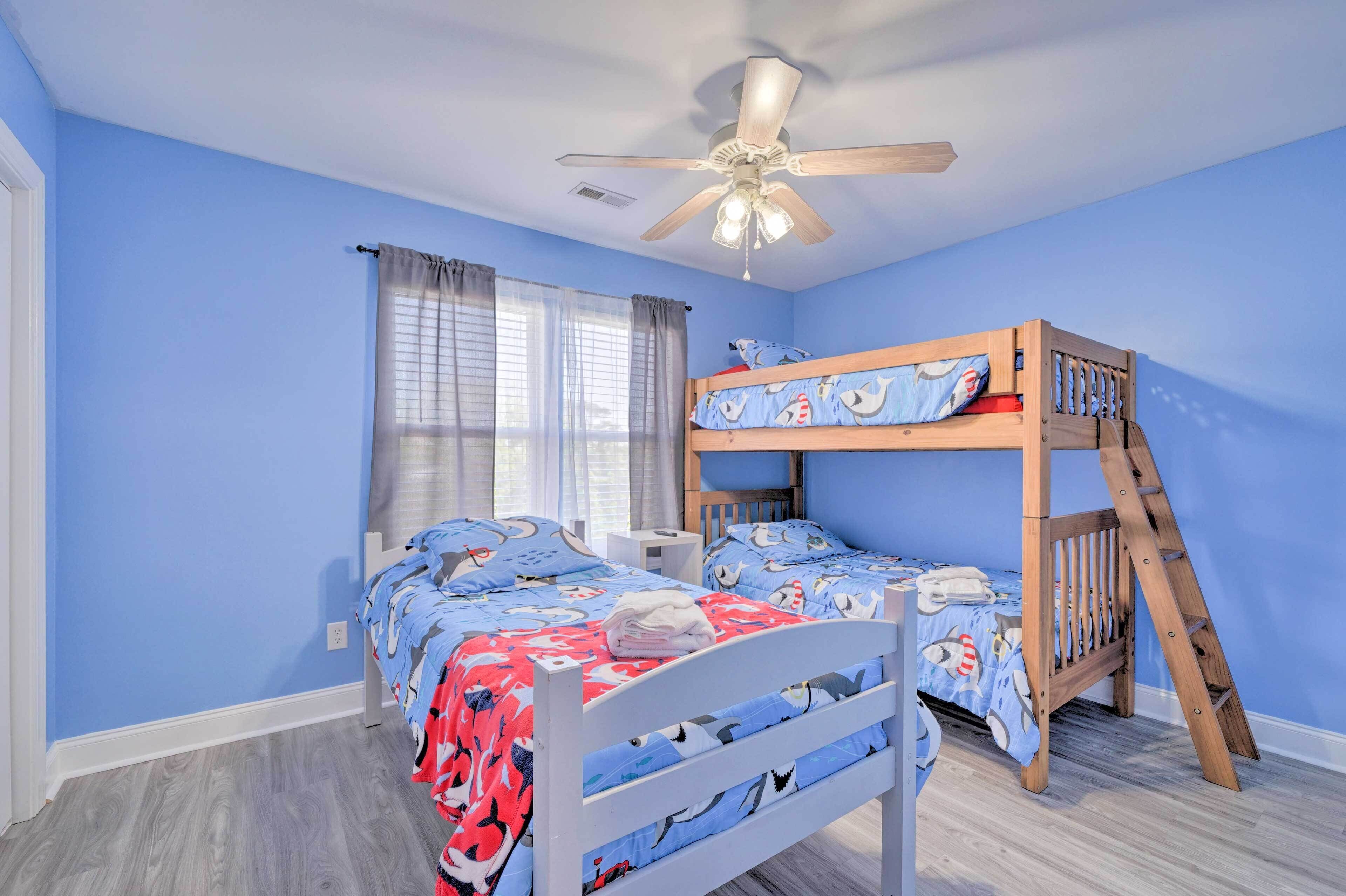 Habitación infantil con literas, ventilador de techo y ventana con cortinas.
