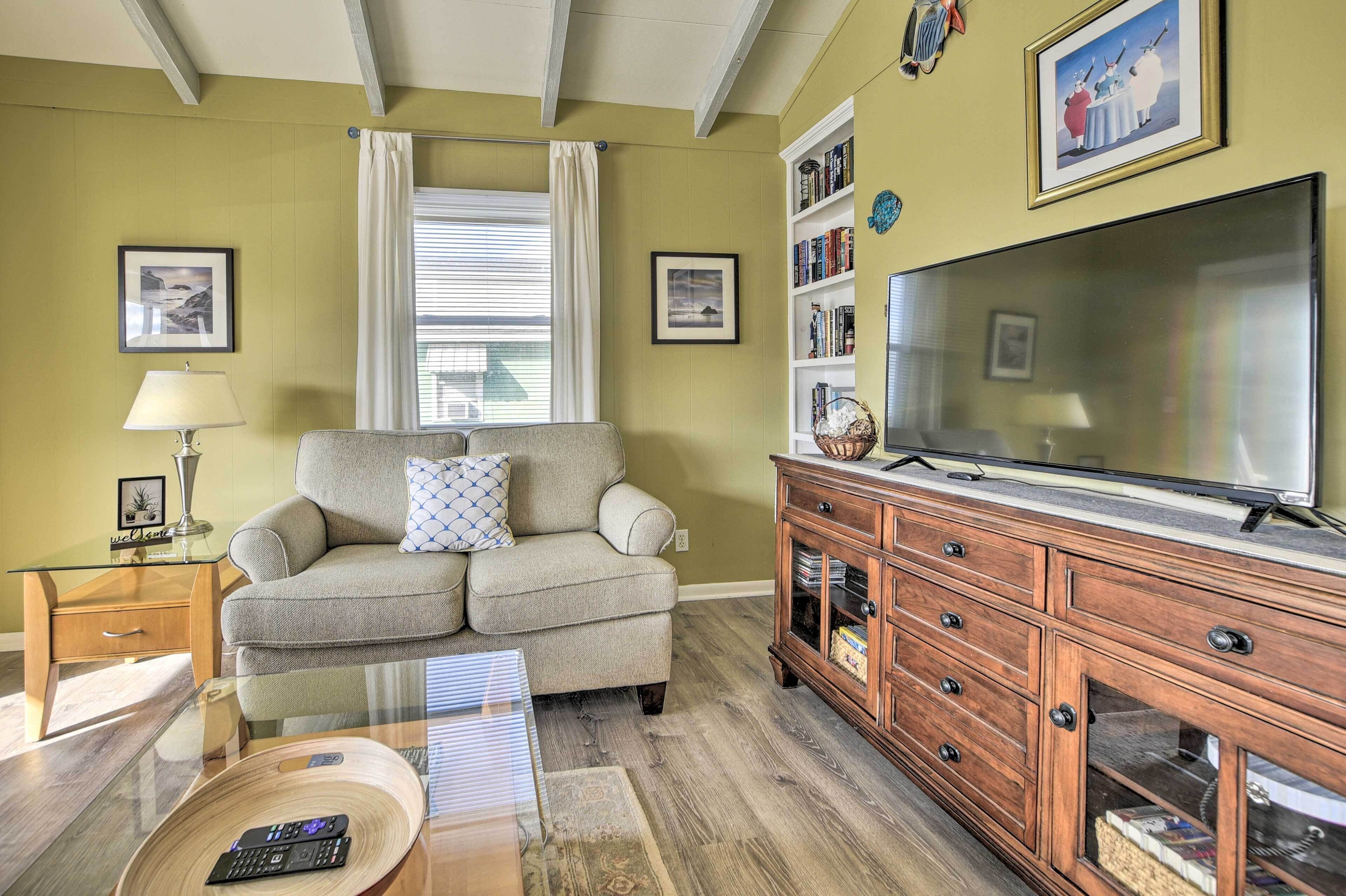 A living room with a sofa, a coffee table, a TV, a bookshelf, and a window with curtains.