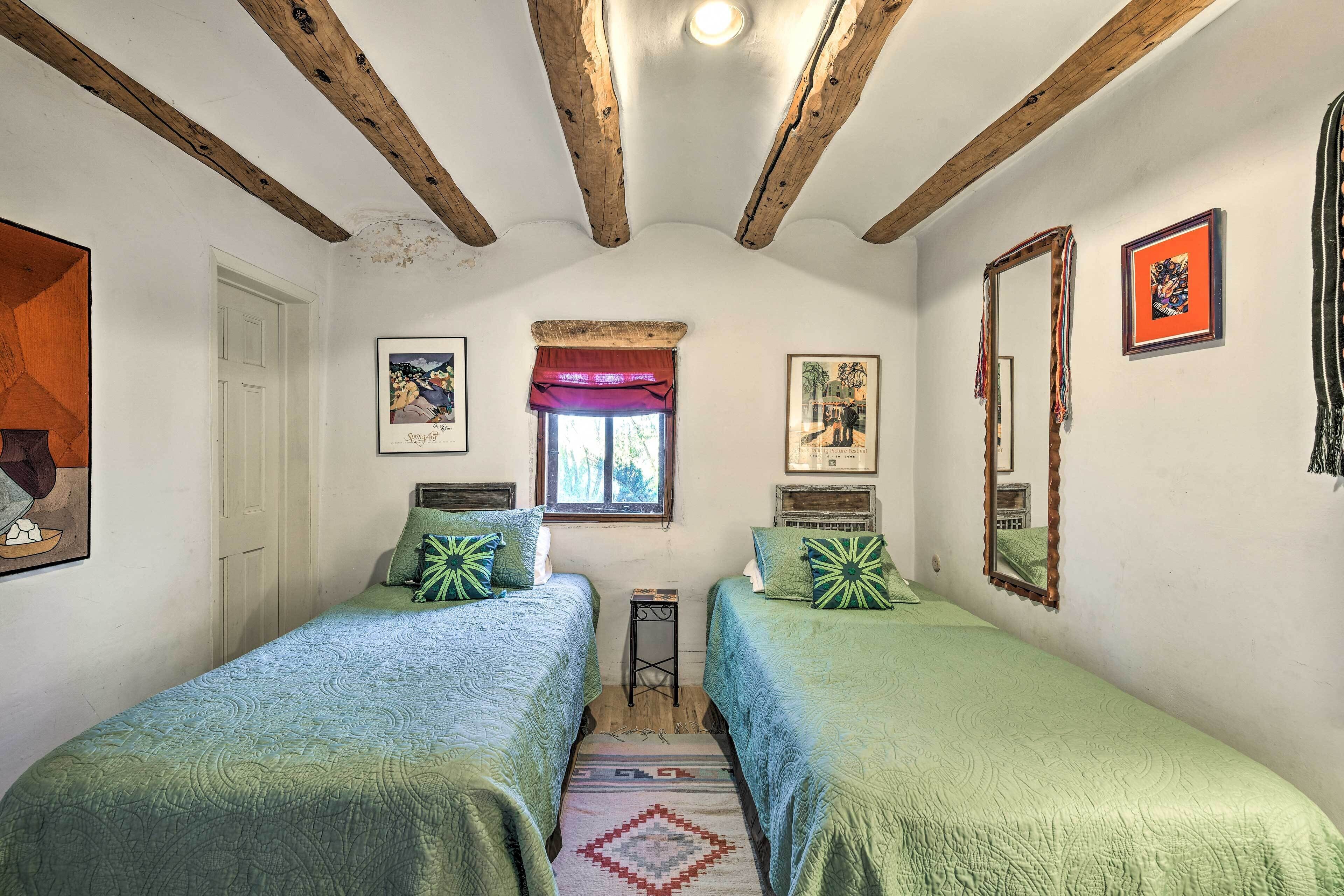 Un dormitorio con dos camas, una ventana con un dosel rojo y un espejo en la pared.