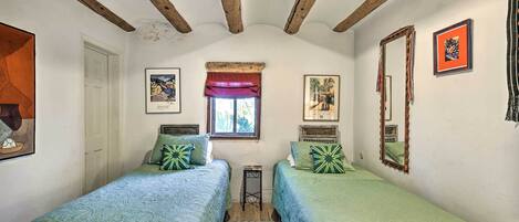 Un dormitorio con dos camas, una ventana con un dosel rojo y un espejo en la pared.