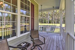 A covered porch with a wooden deck, a chair, and a table. - Oriental House on 1 Acre w/ Wraparound Porch! (Arapahoe)
