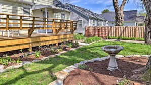 Une terrasse en bois avec un banc, un jardin agrémenté d’un abreuvoir pour oiseaux et une cour clôturée.