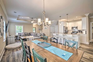 A spacious dining area with a wooden table, blue placemats, and a chandelier. - Charming Pawleys Island Home ~ 4 Mi to Beach! (Pawleys Island)