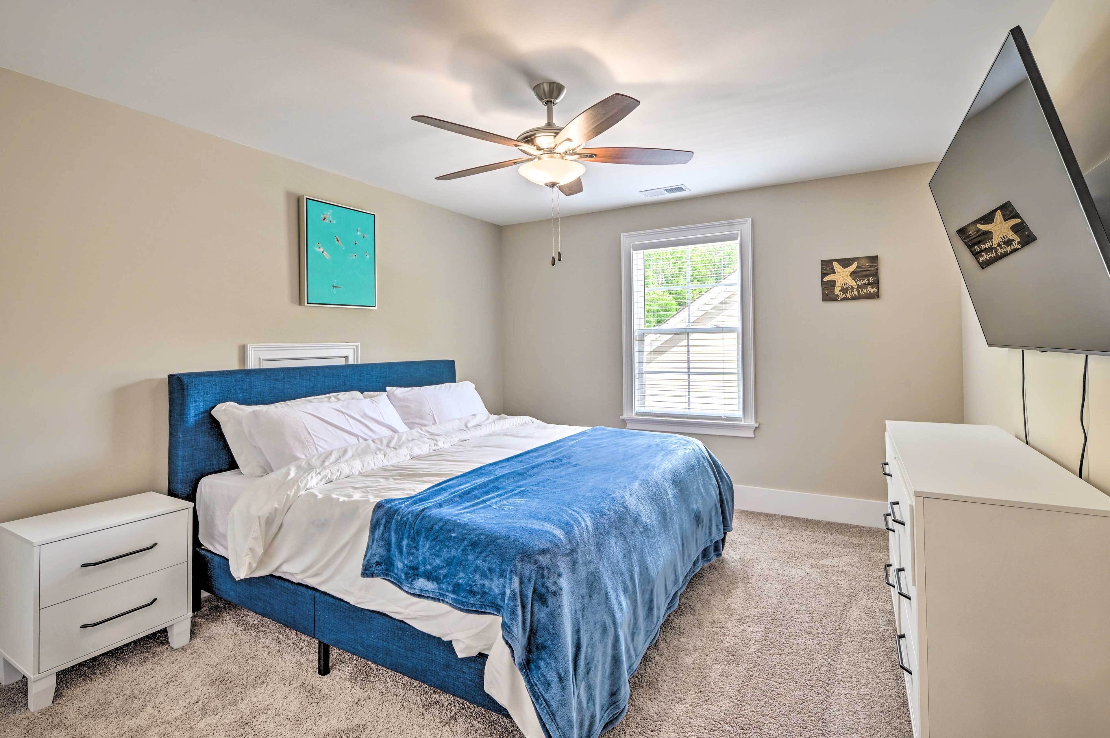 A bedroom with a bed, a nightstand, a dresser, a ceiling fan, a window, and wall decorations.