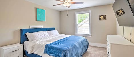 A bedroom with a bed, a nightstand, a dresser, a ceiling fan, a window, and wall decorations.