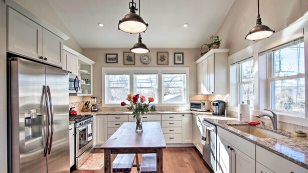 A modern kitchen with stainless steel appliances, white cabinetry, a wooden table, and pendant lighting. - Downtown Lafayette, Colorado, Vacation Rental! (Lafayette)