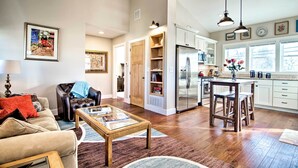 A spacious living room with a leather sofa, a glass coffee table, and a dining area with a wooden table and stools. A kitchen with white cabinets and a stainless steel refrigerator is visible in the background. - Downtown Lafayette, Colorado, Vacation Rental! (Lafayette)