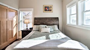 A bedroom with a wooden headboard, a bedside table with a lamp, and a window with a view of trees. - Downtown Lafayette, Colorado, Vacation Rental! (Lafayette)