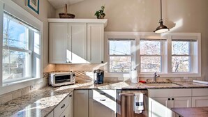 A kitchen with white cabinets, a granite countertop, a toaster, a coffee maker, and a sink. - Downtown Lafayette, Colorado, Vacation Rental! (Lafayette)