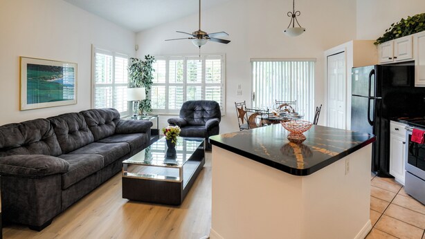 A modern living room with a sofa, coffee table, and a dining area with chairs and a table. - Sunny Port St Lucie Condo: Golf, Swim & Unwind! (Port Saint Lucie)