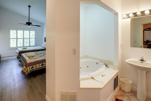 Un dormitorio con cama, ventilador de techo y ventana. También se observa un baño con bañera, lavamanos y espejo.