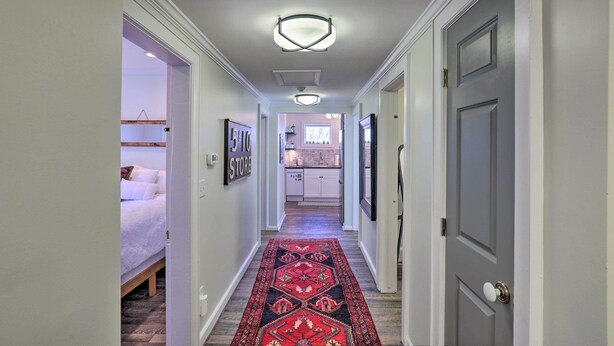 Un pasillo con alfombra estampada, una cama, una cocina y una puerta.