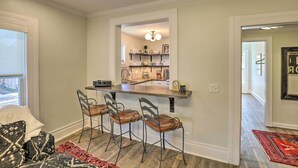 Una cocina con barra, tres taburetes de bar y una encimera con diversos utensilios de cocina.