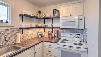 A kitchen with white cabinets, a microwave, a stove, and shelves with dishes and kitchenware.