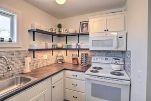 Enjoy cooking in this kitchen with a stainless steel sink, white stove, and microwave, plus ample storage and a window.