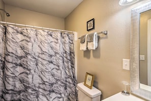 A bathroom with a marble shower curtain, a toilet, a sink with a glass soap dispenser, and a mirror with a textured frame.
