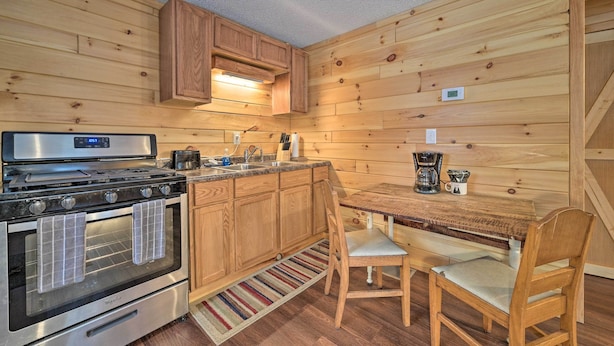 A kitchen with wooden walls, a stove, a coffee maker, and a dining table with chairs.
