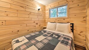 A wooden cabin bedroom with a bed, a window, and a wall-mounted light.